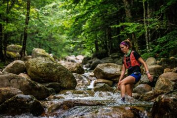 Trail runner crossing a stream in the woods.