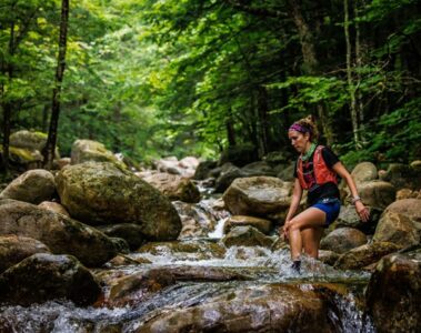 Trail runner crossing a stream in the woods.