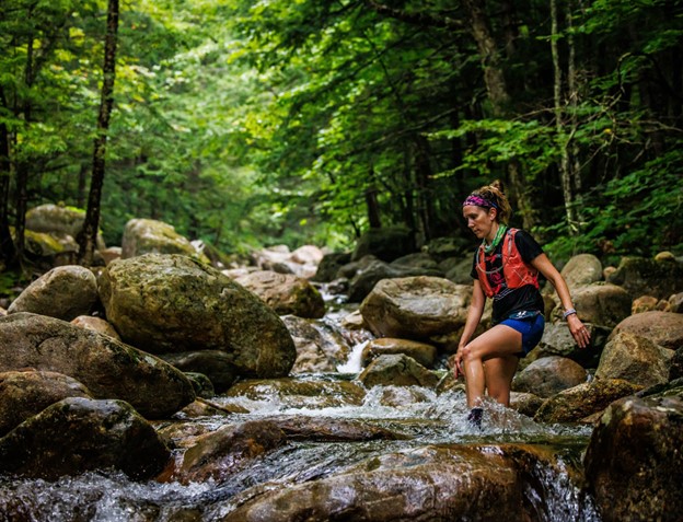 Trail runner crossing a stream in the woods.